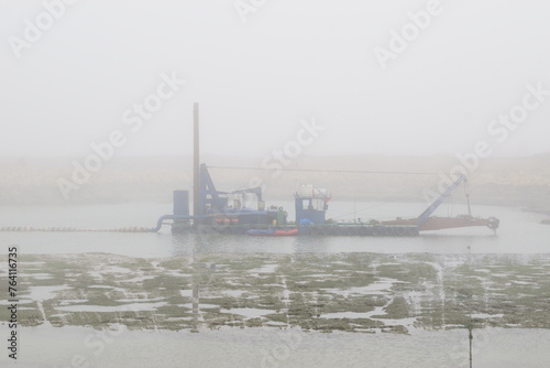 sand excavating and dredging ship ( dredger ship , dredger ) machine removing sand from lake , river;
in a misty day	

