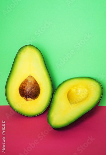 Halves of cut avocado on pink and green background