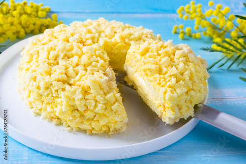 Traditional Italian Mimosa Cake, a popular Italian spring cake with sponge cake and Diplomat cream, light blue background and Mimosa Flours on a table