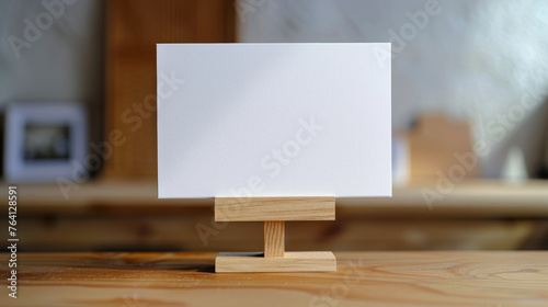 Clean White Blank Card Standing on a Wooden Display Overlooking a Cozy Room © thanakrit