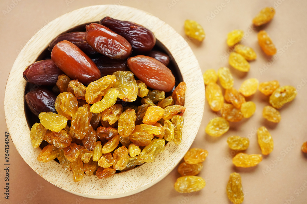 Dried dates and raisins in a wooden plate on a light background Dried dates and raisins in a wooden plate on a light background