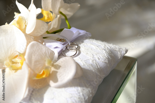 White gold wedding rings. Lying on a white pillow and tied with a white ribbon, surrounded by flowers. Beautiful wedding decor.