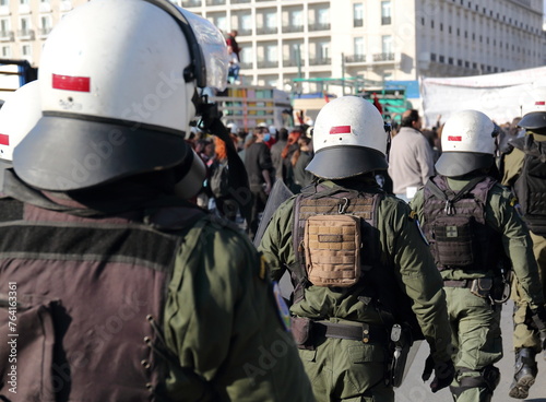 Armed policemen in white helmets on public street demonstration, in background group of protesters in soft focus