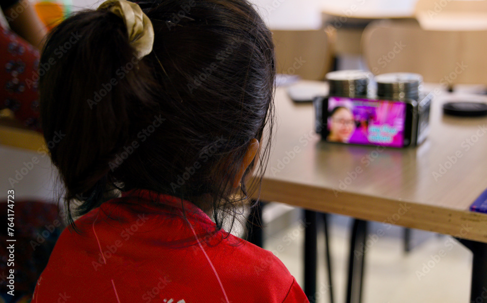 Fototapeta premium Rear view of a girl looking at a mobile phone in a cafe