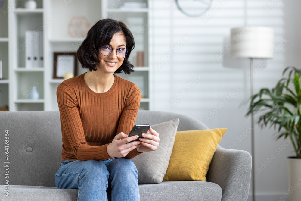 Woman relaxing on sofa at home browsing smartphone