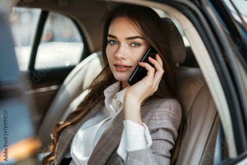 Businesswoman in a suit is sitting in the back seat of a car and talking on mobile phone