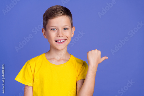 Photo of adorable satisfied small boy wear stylish yellow clothes demonstrate empty space banner isolated on purple color background