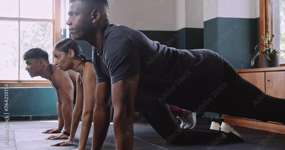A man and a woman workout together in a gym, doing push ups and squats with a group of people. They sit and engage in floor exercises as part of their intense workout routine