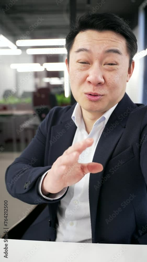 POV Vertical video. Smiling asian businessman in a formal suit talking on video call using a phone in a business office. Mature manager looking at camera. Online chat with a friend or business partner POV Vertical video. Smiling asian businessman in a formal suit talking on video call using a phone in a business office. Mature manager looking at camera. Online chat with a friend or business partner