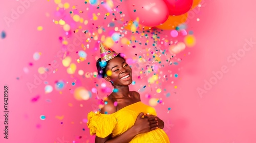 A joyous woman is celebrating with confetti and balloons on a pink background