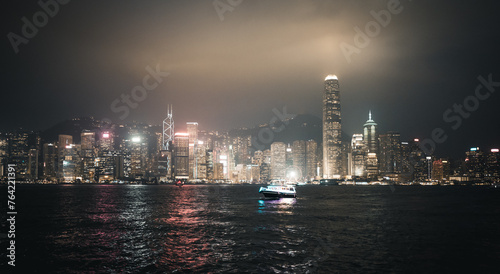 Hong Kong, China : panoramic night shot of Honk Kong from the Tsim Sha Tsui Promenade. Boat and illuminated skyscrapers. people in the foreground.
