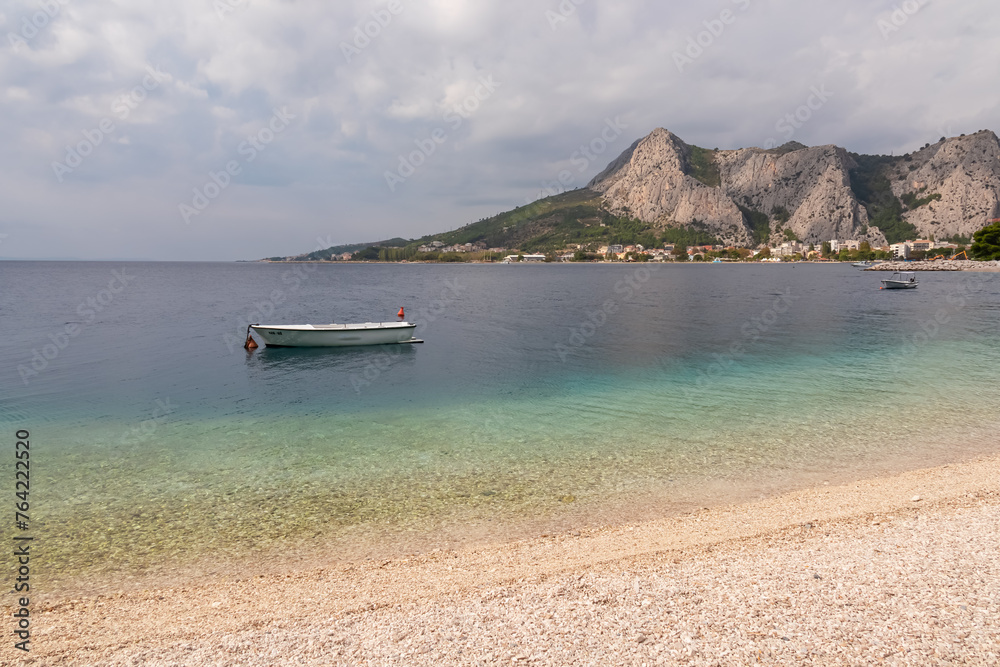 Idyllic sand beach Plaza Brzet in coastal town Omis, Split-Dalmatia, Croatia, Europe. Scenic view of majestic mountains of Dinaric Alps, Balkans. Adriatic Mediterranean Sea. Fishermen boat in lagoon