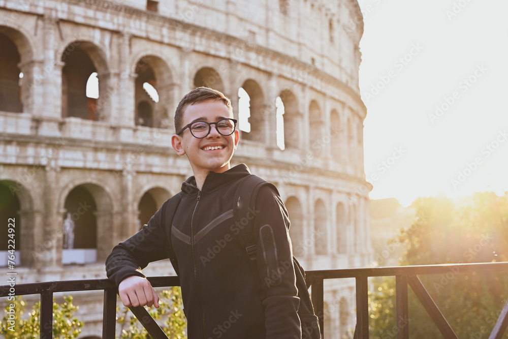 Smiling happy tourist  boy with   eyeglasses  enjoy Colosseum in the old city center of Rome, Italy. Concept  family travel trip.