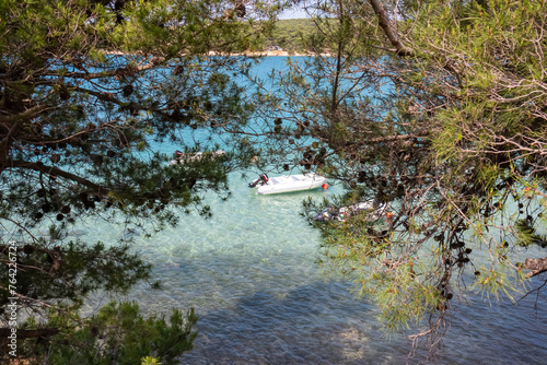 Hanging tree branches overlooking turquoise coloured lagoons with small boat in Medulin, Pomer Bay, Kamenjak nature park, Istria peninsula, Croatia. Coastline Kvarner Gulf, Adriatic Mediterranean Sea photo