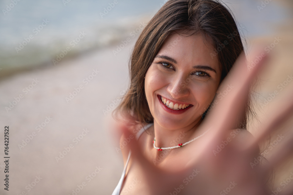 A woman with a red necklace is smiling and waving at the camera