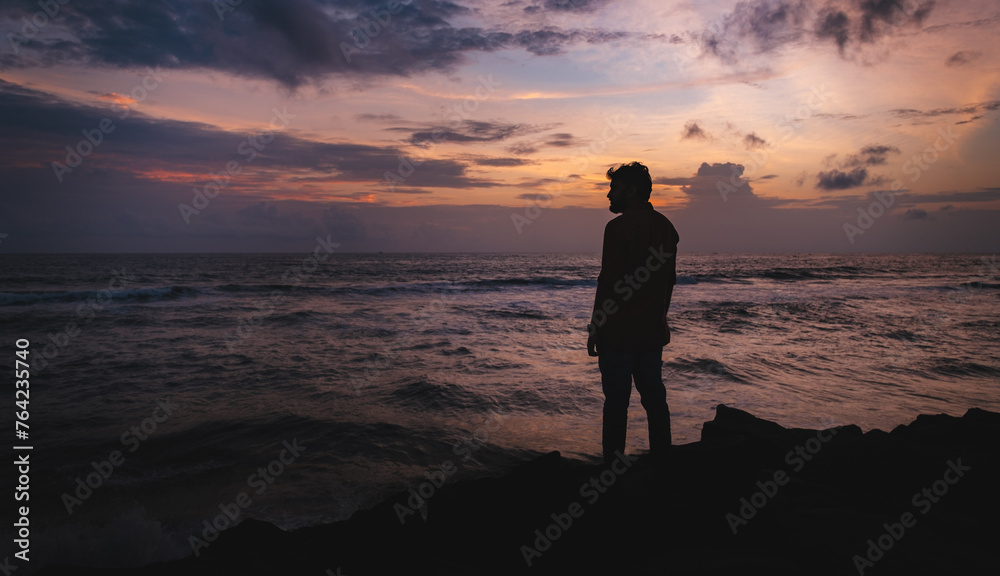 silhouette of man standing on the beach at sunset