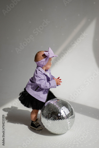 Concept: direction in music, pop music, music for children. Little stylish baby dancing near a silver disco ball