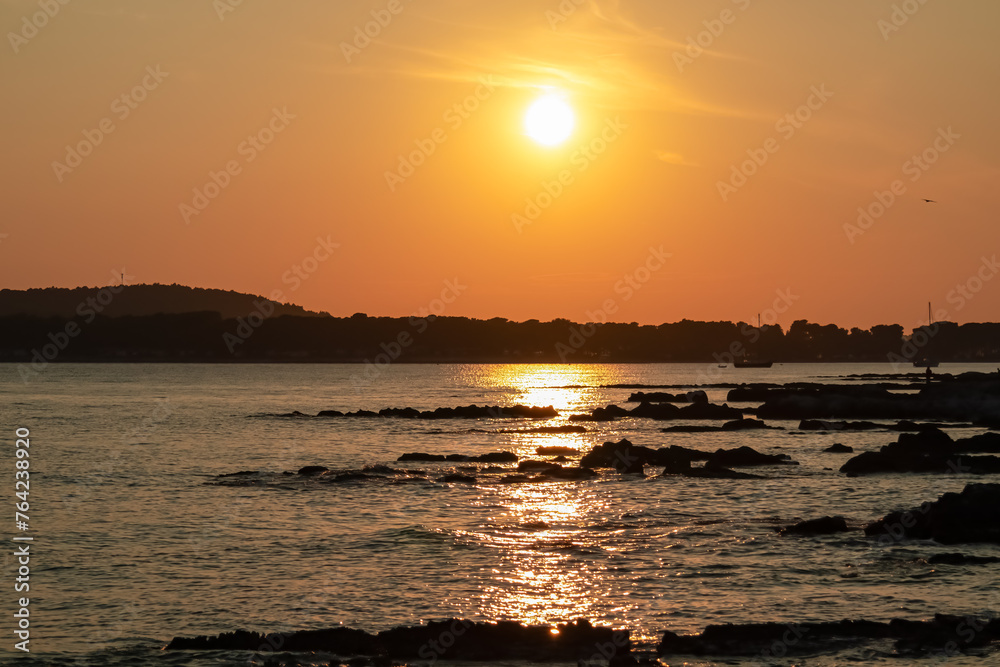 Beautiful sunset at rocky beach in coastal town Medulin, Istria peninsula, Croatia, Europe. Romantic view of rugged coastline Kvarner Gulf in Adriatic Mediterranean Sea in tranquil summer. Tranquility