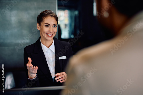 Happy hotel manager talking to  guest at reception desk.