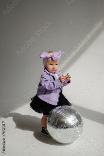 Concept: direction in music, pop music, music for children. Little stylish baby dancing near a silver disco ball