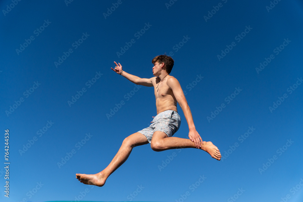 A happy young man jumps and dances against a backdrop of blue sky on a summer day.