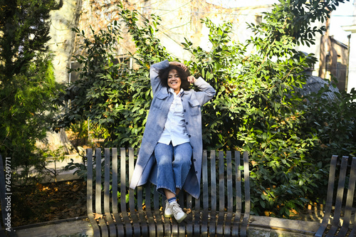 Fashion street style portrait of attractive young natural beauty African American woman with afro hair in blue coat and jeans posing outdoors. Happy tourist laughing walks around the city
