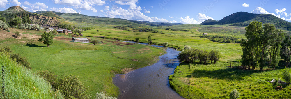 Panoramic view of valley with river bend, green grass, mountains and cloudy blue sky near Deal Gulch from the route CO-317 W. Colorado