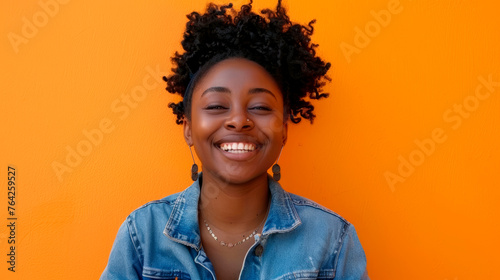 Happy African American woman in denim jacket on orange background. Studio portrait photography with place for text