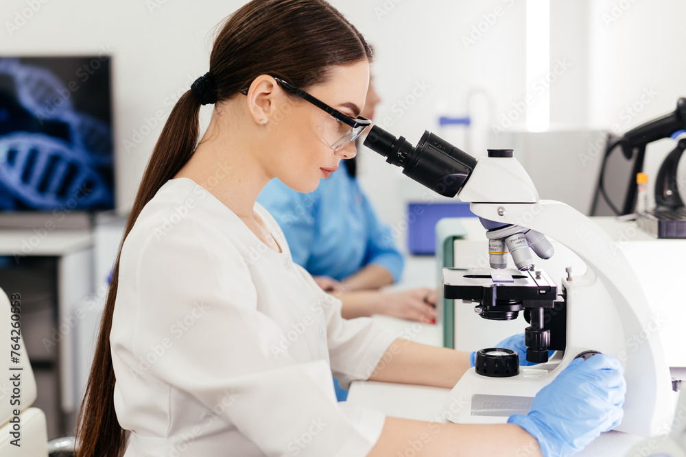 Medical Research Scientist Looks at Biological Samples Under Digital Microscope in Applied Science Laboratory. Beautiful Caucasian Lab Engineer in White Coat Working on Vaccine and Medicine Medical Research Scientist Looks at Biological Samples Under Digital Microscope in Applied Science Laboratory. Beautiful Caucasian Lab Engineer in White Coat Working on Vaccine and Medicine
