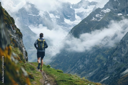 An athletic man runs along a solitary mountain trail, with the dramatic backdrop of towering peaks shrouded in mist, embodying the essence of solitude and endurance in nature's grandeur
