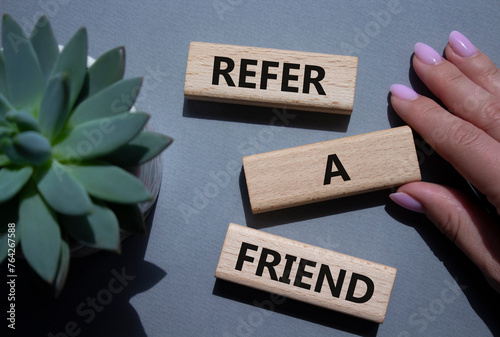 Refer a Friend symbol. Concept words Refer a Friend on wooden blocks. Beautiful grey background with succulent plant. Businessman hand. Business and Refer a Friend concept. Copy space.