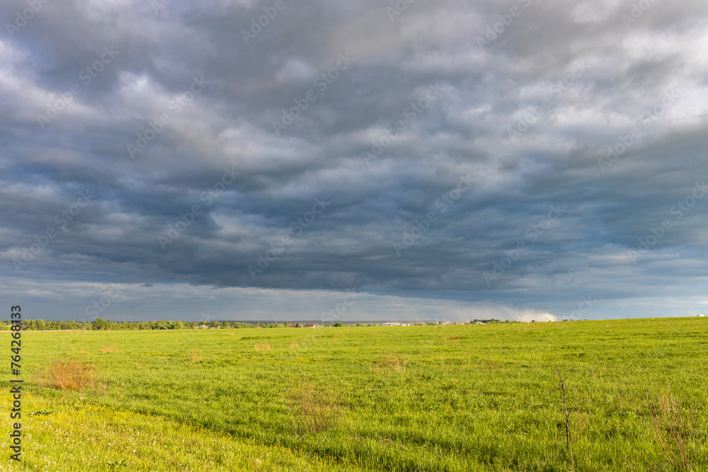 Sunny landscape against a dramatic sky, countryside in early spring, young green grass in a field Sunny landscape against a dramatic sky, countryside in early spring, young green grass in a field