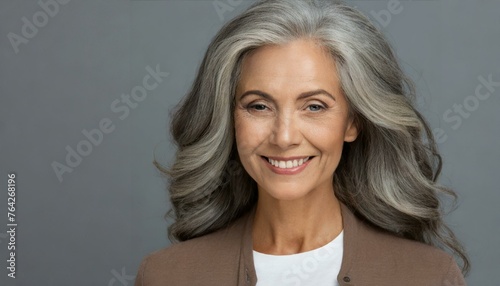 elder woman with smooth healthy face skin and gorgeous gray curly hair smiling confidently isolated on gray background, with copy space 