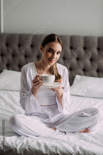 The image is of a woman sitting on a bed holding a cup of coffee 6582.