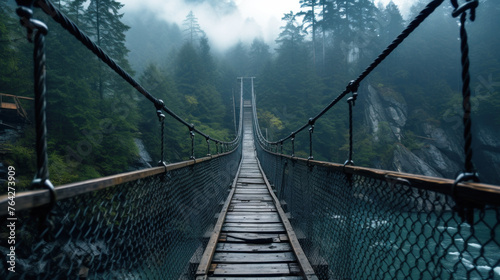 Old suspension bridge in misty forest, vintage hanging wood path over river in dark foggy woods. Concept of travel, journey, nature, adventure and wanderlust photo