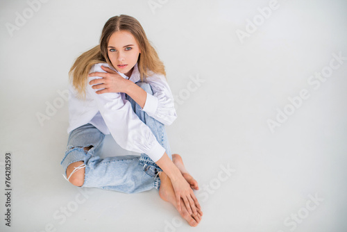 A woman is sitting on the floor in jeans and a white shirt.