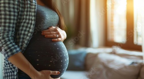 Close up of a pregnant woman holding her belly at home, close up shot, blurred background with copy space. Pregnancy background