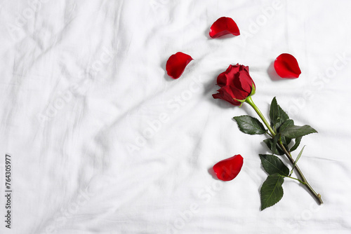 Fototapeta Naklejka Na Ścianę i Meble -  Honeymoon. Red rose and petals on bed, top view. Space for text