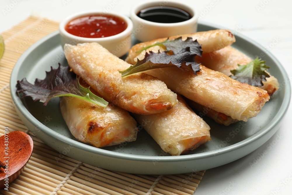 Tasty fried spring rolls, lettuce and sauces on white marble table, closeup