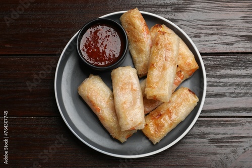 Tasty fried spring rolls and sauce on wooden table, top view