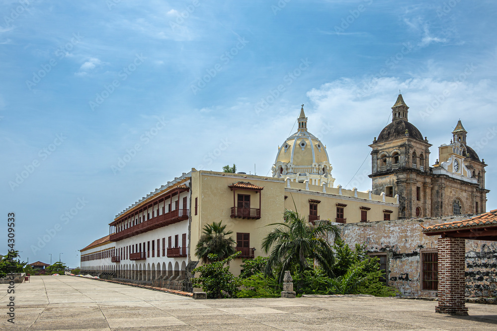 Cartagena, Colombia - July 25, 2023: Santuario de San Pedro Claver church towers, historic front facade with cloister and museum buildings on side under blue cloudscape. Green foliage in front