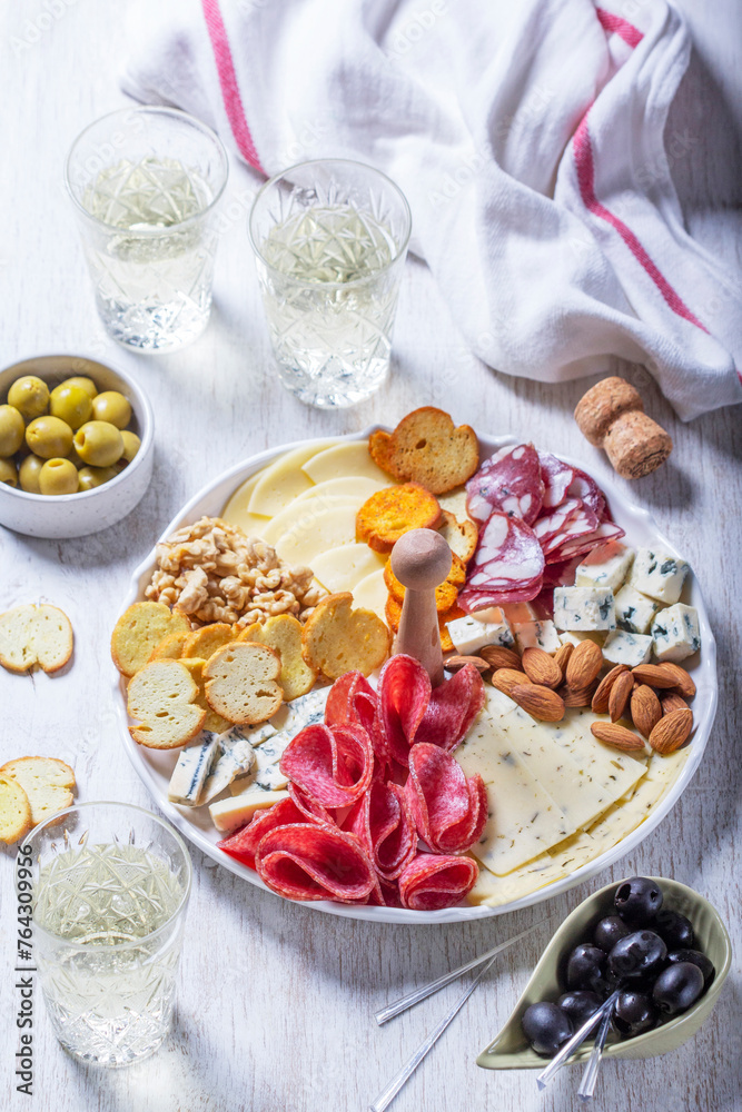 Aperitif, champagne and snack of sausage, cheese, nuts, olives and crackers on a light background.