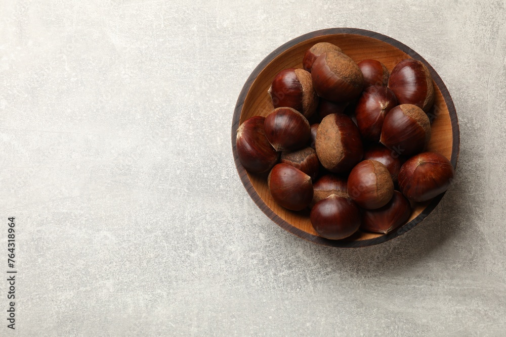 Obraz premium Roasted edible sweet chestnuts in bowl on light grey table, top view. Space for text