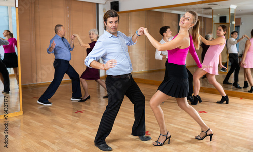 Positive man and woman dancing energetic upbeat jive as couple during group training in dance studio..
