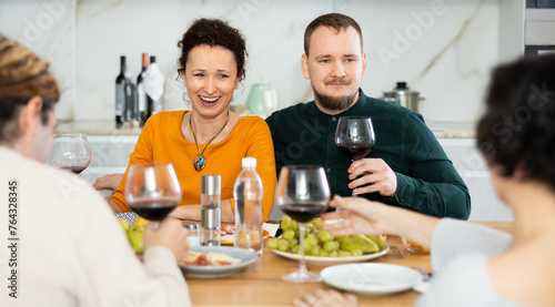 Two married couples are sitting at table, enjoying food and wine, chatting, talking, laughing. In homely atmosphere, friends celebrate anniversary
