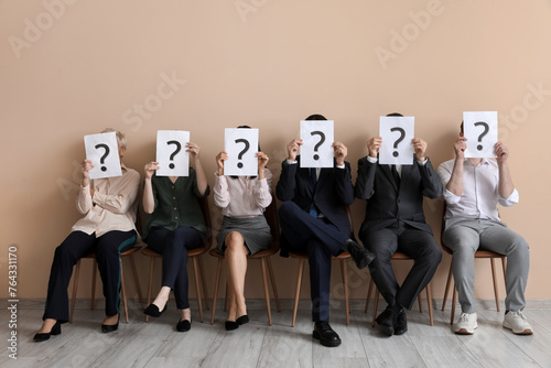 Applicants holding paper sheets with question marks near beige wall