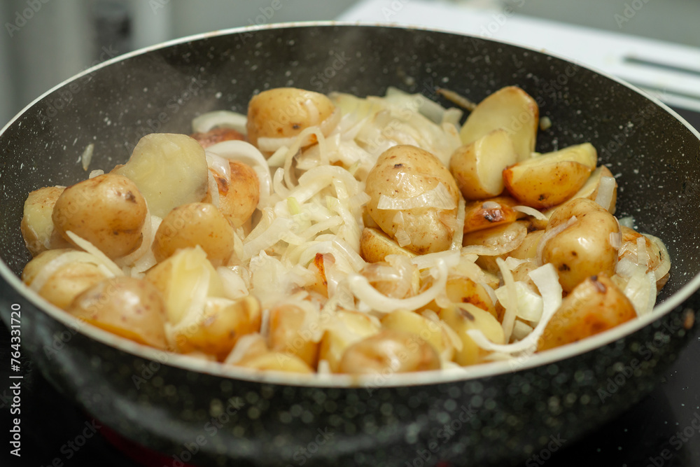 A black pan with a white lid is filled with potatoes and onions A black pan with a white lid is filled with potatoes and onions