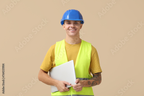 Young male engineer with laptop on beige background
