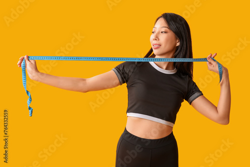 Beautiful young Asian woman with measuring tape on yellow background. Weight loss concept