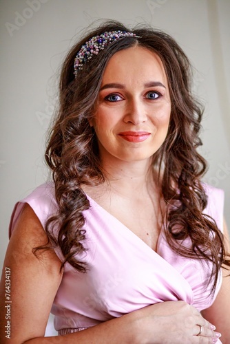 Portrait of a beautiful young woman with long brown curly hair in a pink dress